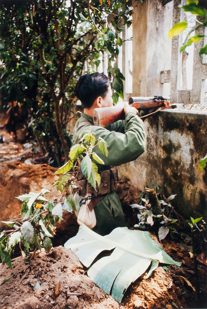 Với lá ngụy trang dắt vào trang phục, người chiến sĩ Giải phóng điểm hỏa qua tường rào một ngôi nhà gần nhà thờ Chính tòa Huế.
