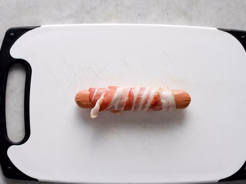 Đặt xúc xích lên trên lát thịt và tiến hành cuộn đều từ đầu cho đến hết. Bạn có thể dùng tăm để ghim thịt, xúc xích ở hai đầu.