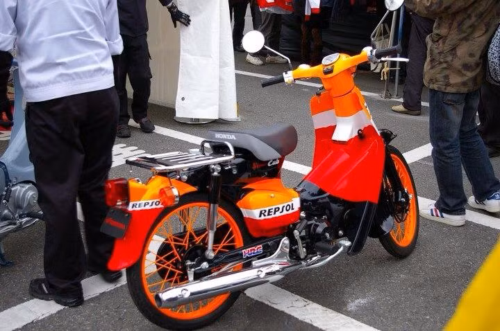 Honda Cup độ Repsol nổi bật với dàn áo đỏ-da cam sặc sỡ cùng những phụ kiện đồng màu đi cùng.