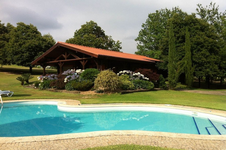 Nhà gỗ được bao quanh bởi một khu vườn gồm cây trưởng thành và hoa mọc cao tầm trung, dãy ghế nghỉ và một bể bơi xanh mát