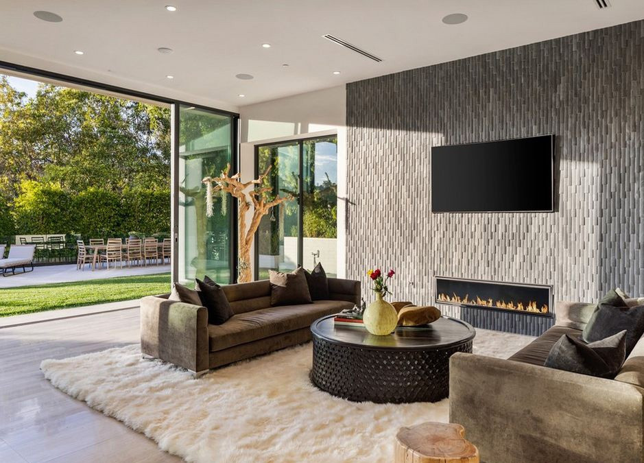 Phòng khách trang nhã, được liên kết với sân vườn nhờ hệ cửa kính. Sàn gỗ cứng và lò sưởi khiến không gian này ấm cúng hơn.