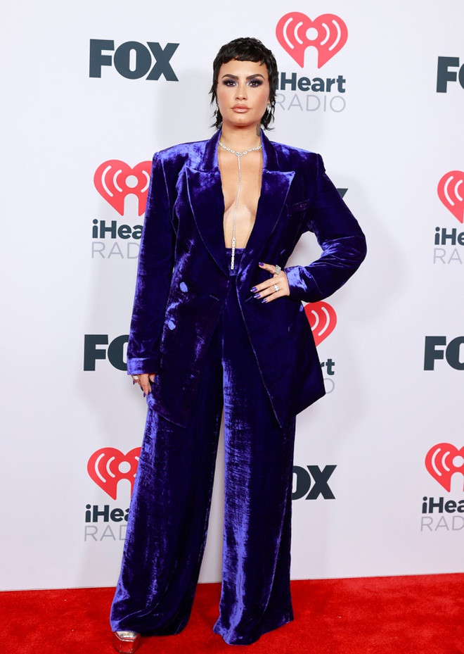 br/> Demi Lovato góp mặt tại lễ trao giải iHeart Radio với hình ảnh nam tính. Cô diện suit phom dáng quá khổ, cùng cầu vai dựng phồng cứng cáp. Nữ ca sĩ khoe cơ thể gợi cảm bằng cách không cài nút áo blazer. Nhằm tránh hình ảnh phản cảm, Demi kết hợp thêm vòng cổ kim cương bản mảnh với chiều dài đến lưng quần.