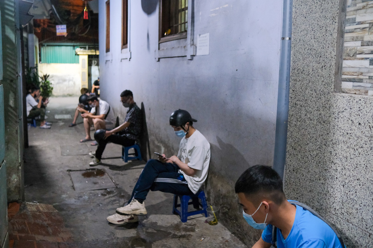 Các shipper ngồi hàng dài khi đồng hồ đã điểm gần 0h. Thời điểm này là lúc nhộn nhịp nhất do các trận đấu Euro 2020 diễn ra vào khung 23h và 2h. Trong thời điểm dịch bệnh còn diễn biến phức tạp, các shipper được yêu cầu giữ khoảng cách và đeo khẩu trang khi chờ đơn.