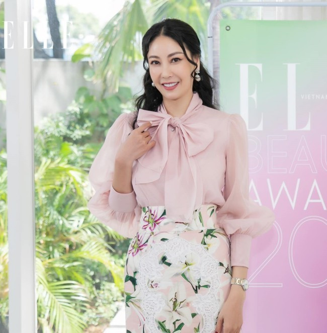 Giám khảo Miss World Việt Nam ngọt ngào, thanh lịch với áo voan thắt nơ màu hồng pastel và chân váy bút chì thêu hoa lyly trắng. Người đẹp để tóc xoăn nhẹ, chọn bông tai màu bạc và đồng hồ để hoàn thiện outfit của mình.