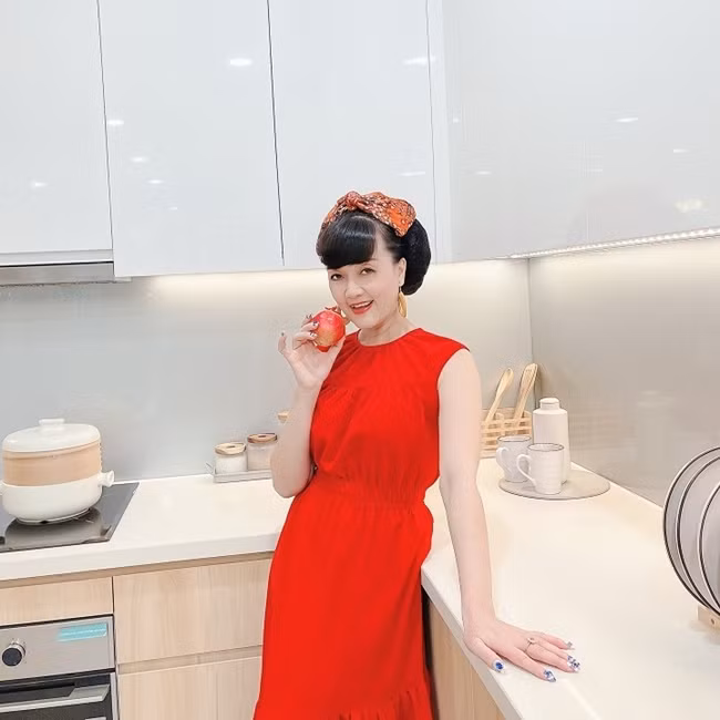 Vân Dung chọn băng đô hoa và bông tai màu vàng nâu để kết hợp váy liền đỏ ngắn tay và chi tiết hạ eo giúp người mặc thêm thon gọn.