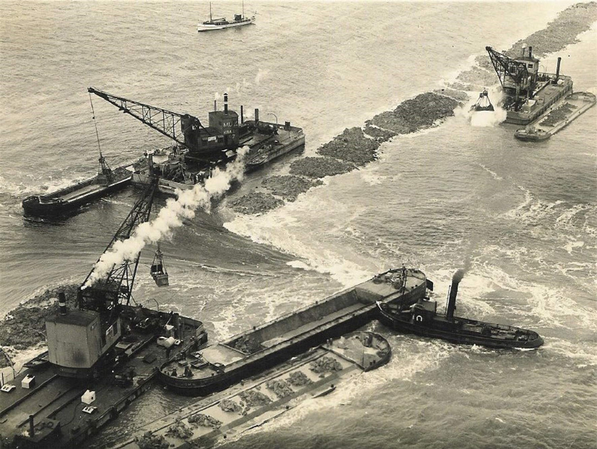 br/> Thi công được tiến hành từ bốn điểm, chân đê cơ bản được mở rộng dần bằng cách đóng cọc, người Hà Lan đã múc các khối sét băng hà từ đáy biển và dựng thành 2 hàng song song làm tường đê, sau đó, dùng tàu chở đá, cát và đất sét đổ vào giữa 2 bức tường.