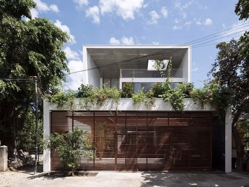 Thêm một mẫu nhà mái bằng theo phong cách hiện đại. Cổng nhà được trồng thêm cây xanh tạo độ che phủ làm dịu bớt cái nóng. 