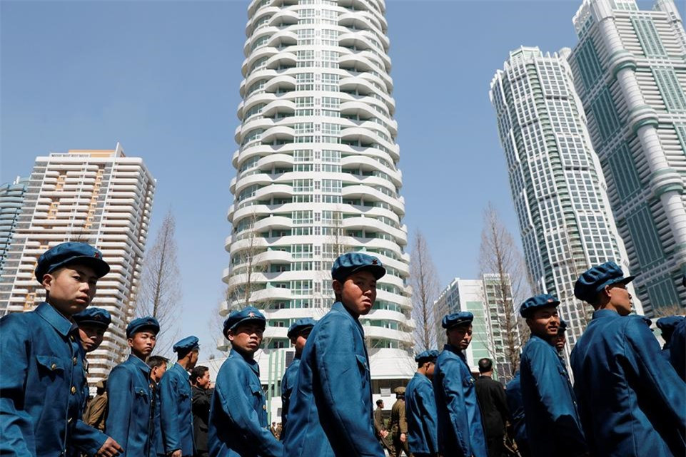 Các công nhân trong bộ đồng phục đi bộ qua những tòa nhà cao tầng nằm trong một khu dân cư mới xây dựng trên đường Ryomyong tại Bình Nhưỡng.