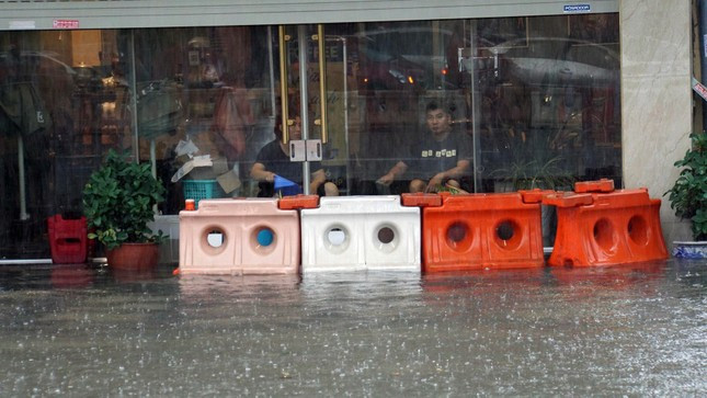 Chủ một cửa hàng cà phê trên phố Lạch Tray dùng dải phân cách bị đánh dạt che chắn sóng nước tràn vào nhà. Đồng thời, thay nhau dùng gáo tát nước ra khỏi cửa hàng.