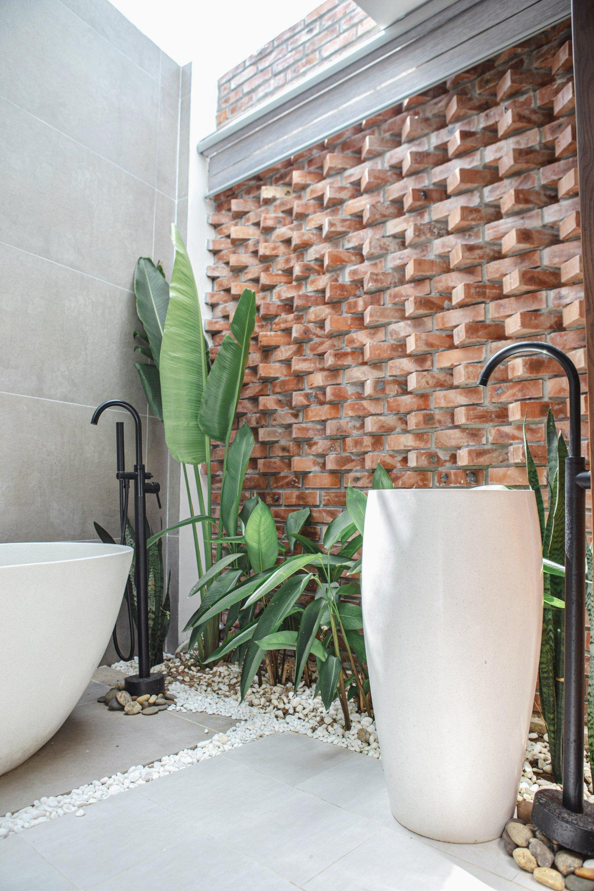 Mảng tường phòng tắm để gạch đỏ, xây theo kiểu đặc biệt, xếp đặt zíc zắc. Dưới bồn tắm trải sỏi trắng mát-xa, bố trí cây xanh để gia chủ có cảm giác hòa mình cùng thiên nhiên.