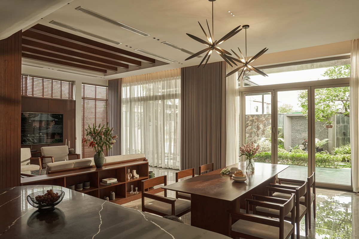 Khu vực tiếp khách ngăn với khu bếp bằng một kệ tủ nhỏ tiện dụng. Trần nhà được ốp gỗ, điểm xuyết hệ thống đèn trang trí tinh tế.