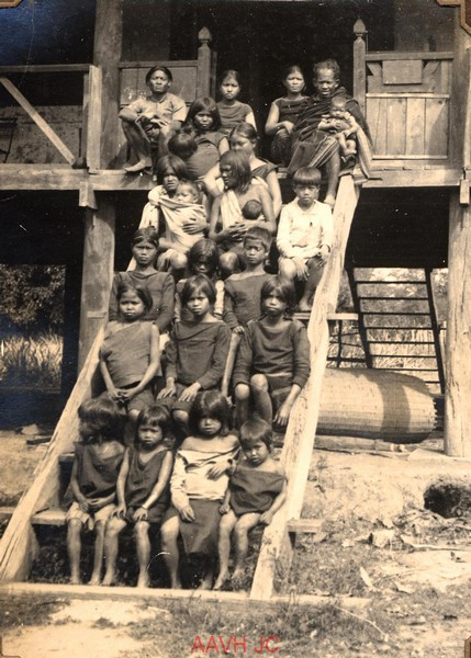 Phụ nữ và trẻ em Ba Na ngồi trên cầu thang của một nhà sàn.