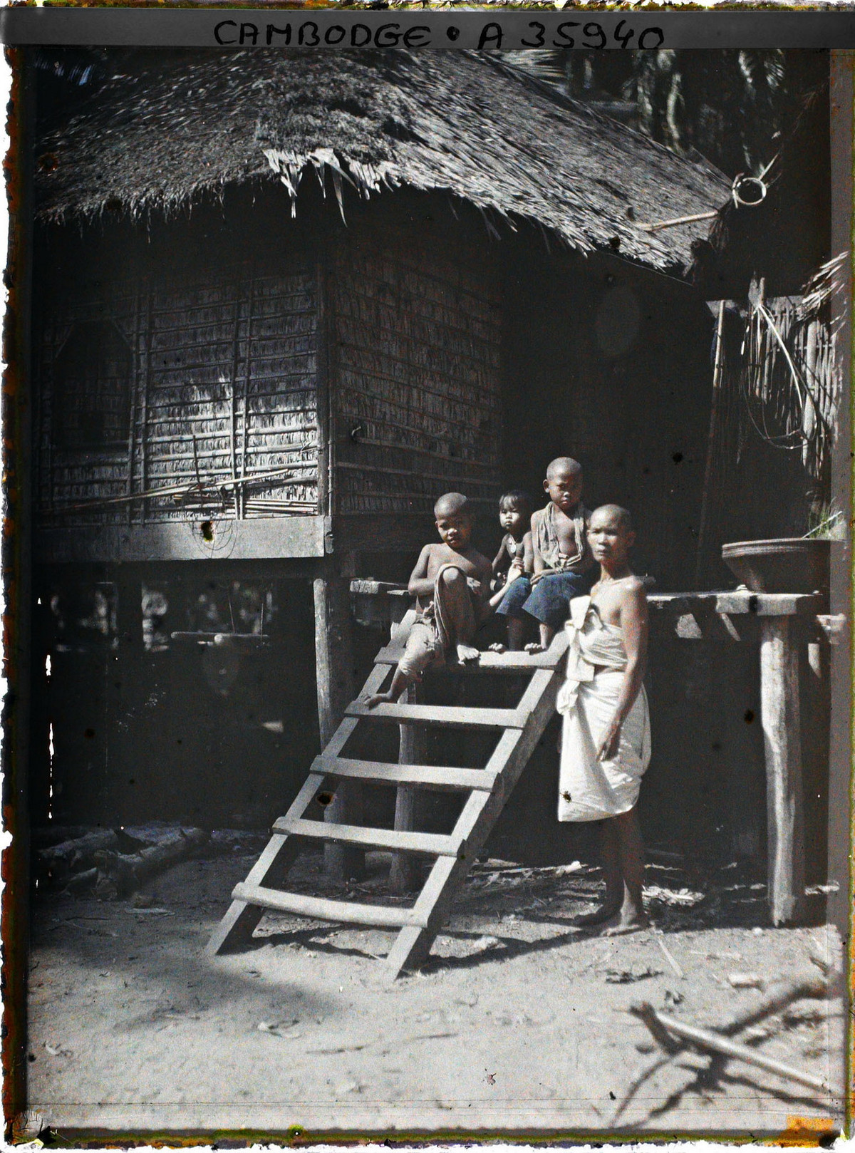 Người phụ nữ và những đứa trẻ bên cầu thang dẫn lên một ngôi nhà sàn.
