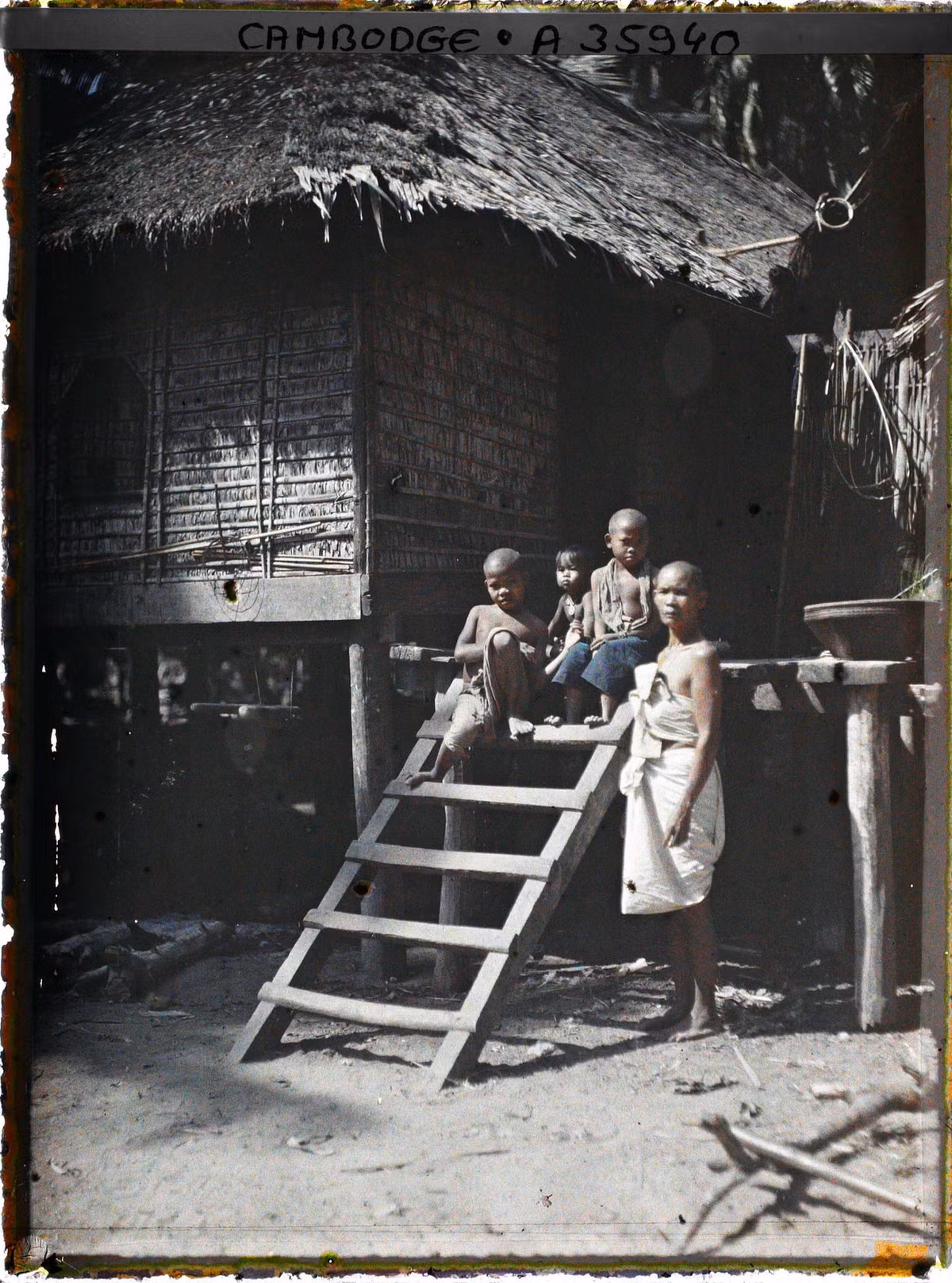 Người phụ nữ và những đứa trẻ bên cầu thang dẫn lên một ngôi nhà sàn.