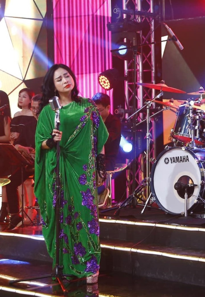 Chiếc váy nhung dài đính hoa lay ơn tím dọc thân độc và lạ đúng “chất” Thanh Lam, cùng chi tiết bèo nhún đã làm điểm nhấn cho thiết kế được dành riêng cho cô. Đôi găng tay ren có phần “sến” lại là chi tiết độc đáo mà nữ ca sĩ thêm vào trang phục trình diễn của mình.