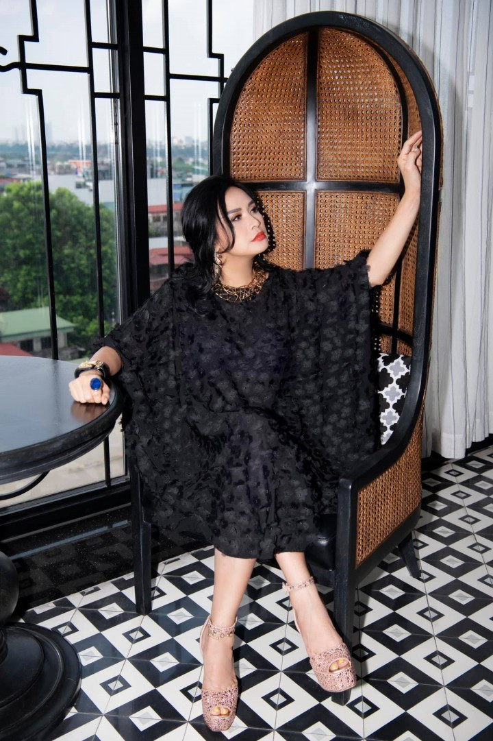 Nữ ca sĩ gốc Hà Nội bí ẩn trong chiếc váy cánh dơi màu đen. Trên nền vải in hoa nổi, cô chọn chiếc vòng cổ mảnh màu gold và bông tai dài giúp trang phục trở nên nổi bật, phù hợp với kiểu tóc xoăn nhẹ và lối trang điểm nhấn vào mắt, môi tô đậm của cô.