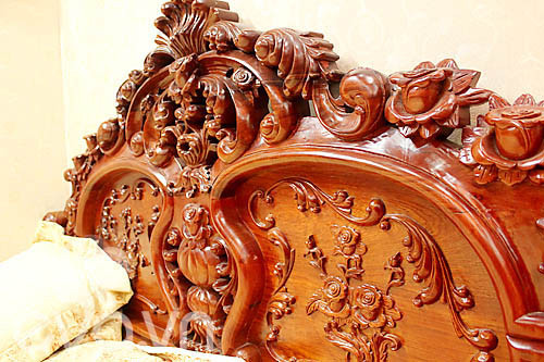 Phần đầu giường được trạm chổ kỳ công những đóa hoa hồng. Ngoài ra, chủ nhân còn rất tinh tế khi sử dụng giấy dán tường màu vàng nâu hòa hợp với sắc gỗ ấm áp của bộ giường tủ theo phong cách Hoàng hậu.