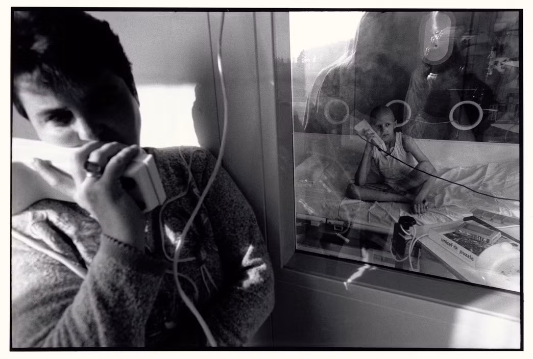 Một người mẹ trò chuyện với con gái qua điện thoại ở bệnh viện Ưng thư Trẻ em tại Minsk, Belarus. Con gái bà phải ở trong phòng cách ly trogn quá trình điều trị ung thư bằng ghép tủy xương. Ảnh: Paul Fusco/ Magnum Photos.