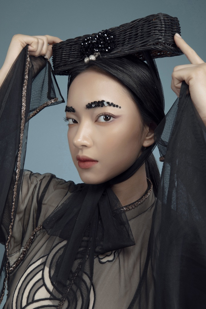 Lối trang điểm tông màu trầm cùng lông mày đính sequins là những điểm nhấn mang hơi thở thời đại, trẻ trung và phá cách, bên cạnh mũ đội đầu kết từ cói truyền thống.