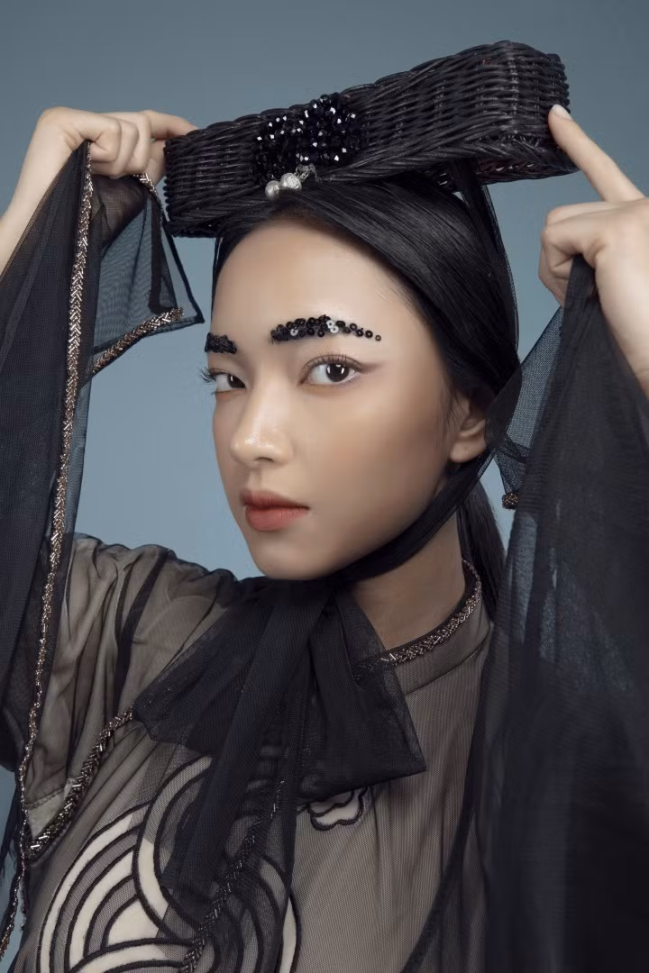 Lối trang điểm tông màu trầm cùng lông mày đính sequins là những điểm nhấn mang hơi thở thời đại, trẻ trung và phá cách, bên cạnh mũ đội đầu kết từ cói truyền thống.