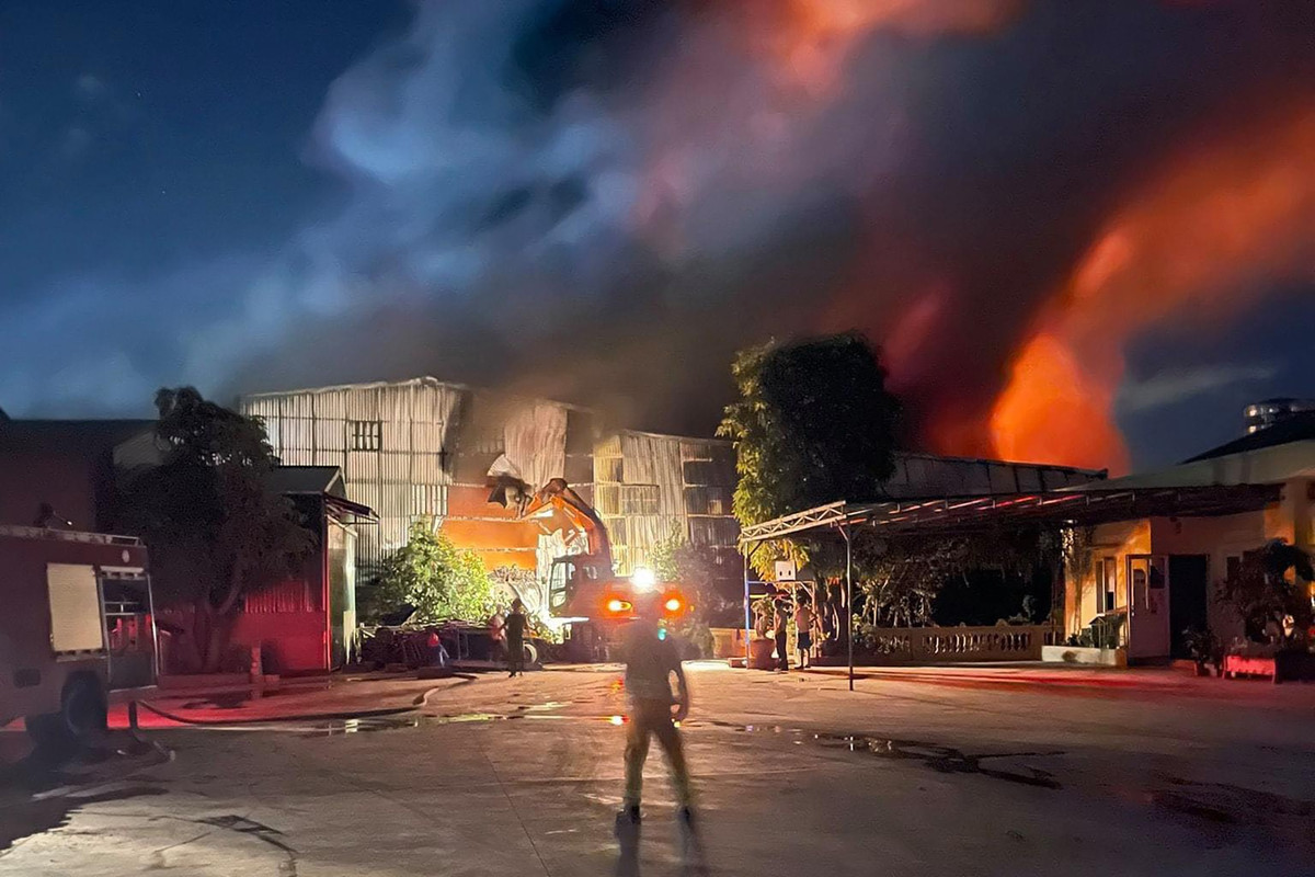 Một chiếc máy cẩu cố gắng phá tường rào nhà kho để lực lượng cứu hộ dập lửa.