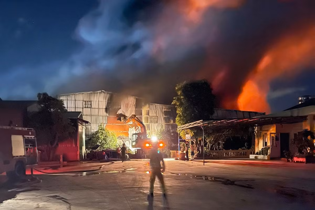 Một chiếc máy cẩu cố gắng phá tường rào nhà kho để lực lượng cứu hộ dập lửa.