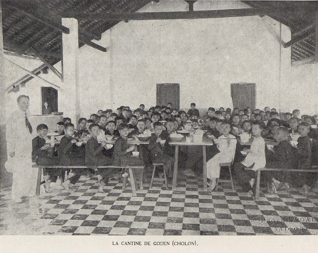 Một giáo viên đứng bên các học sinh tại nhà ăn của một trường học ở quận Gò Đen, tỉnh Chợ Lớn cũ.