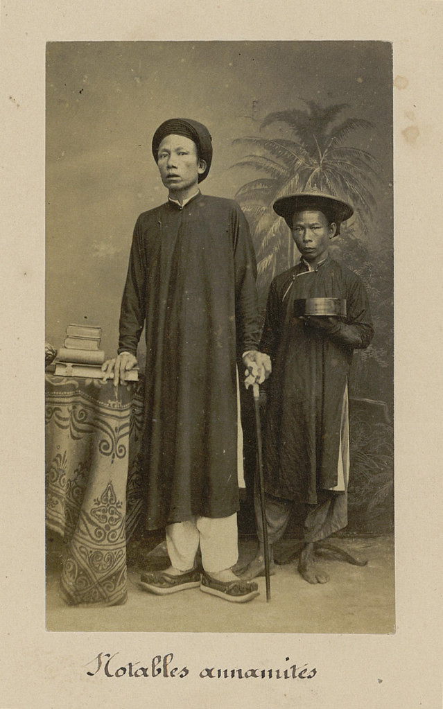 Người đàn ông quý tộc và và gia nhân bưng tráp đứng cạnh.