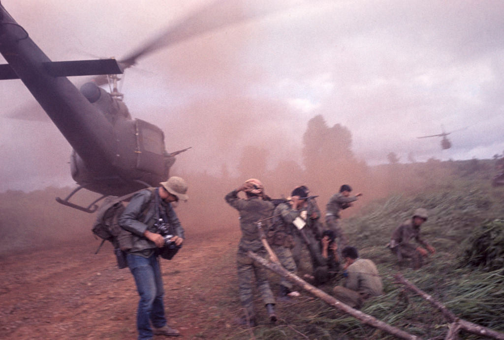 Phóng viên chiến trường phương Tây đứng cạnh một bãi đáp trực thăng dã chiến mịt mù bụi đất do luồng gió từ cánh quạt chiếc trực thăng đang hạ cánh. Ảnh: Jean-Claude Sauer.