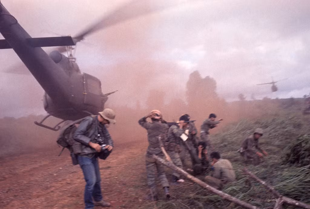 Phóng viên chiến trường phương Tây đứng cạnh một bãi đáp trực thăng dã chiến mịt mù bụi đất do luồng gió từ cánh quạt chiếc trực thăng đang hạ cánh. Ảnh: Jean-Claude Sauer.