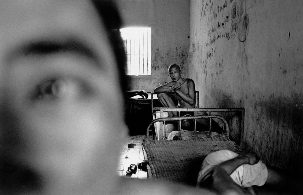 Một bệnh nhân nhìn thẳng vào ống kính máy ảnh qua ô cửa nhỏ. Đến năm 1990, Bệnh viện Tâm thần Hà Nội có 200 giường bệnh. Các tiện nghi cơ bản ở nơi đây khá thiếu thốn và tình trạng quá tải thường xảy ra, theo lời nhiếp ảnh gia Larry Towell. Ảnh: Larry Towell/ Magnums.