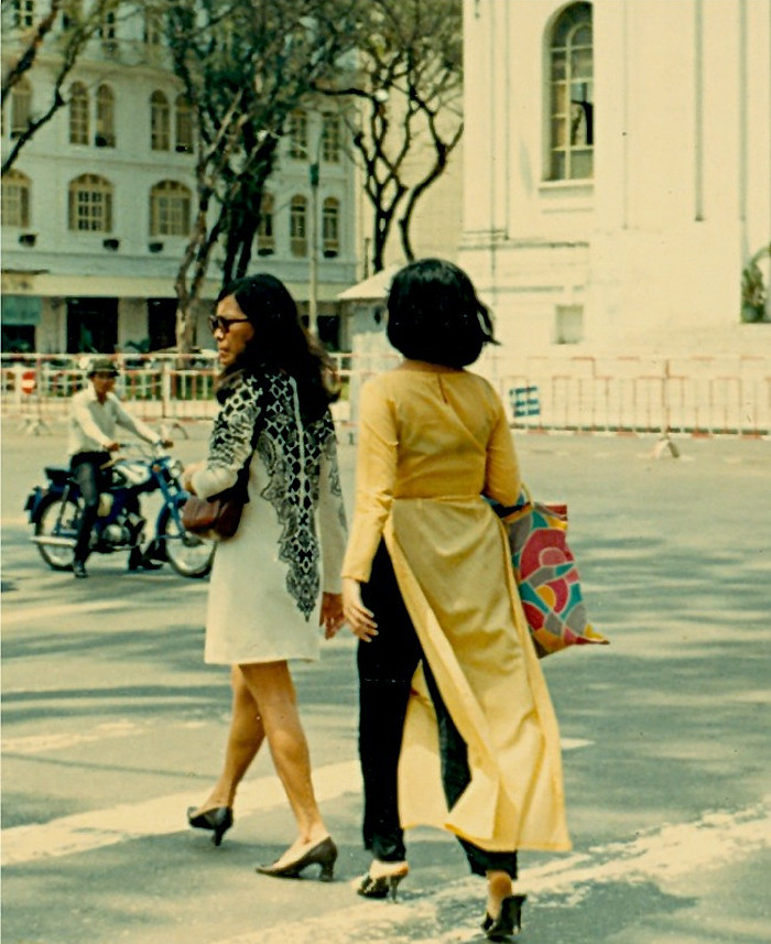 Hai phụ nữ, một mặc áo dài truyền thống, một mặc âu phục bước qua trước nhà Hạ viện.