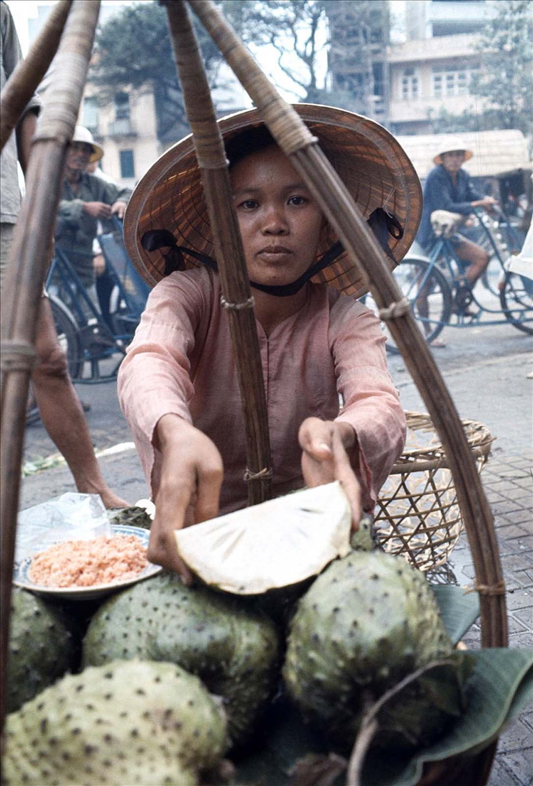 Cô gái bán mãng cầu xiêm mời khách một miếng mãng cầu đã cắt, bên cạnh lả đĩa muối ớt.