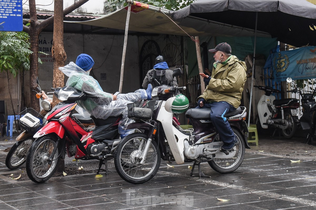 Tài xế lái xe ôm mặc áo mưa kín mít túm tụm trò chuyện chờ khách.