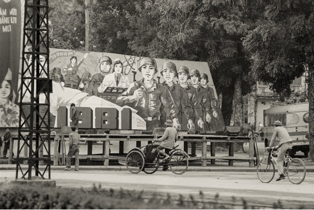 Sân khấu ngoài trời được dựng bên bờ hồ Hoàn Kiếm, chỗ vườn hoa tượng đài Quyết tử, Hà Nội giai đoạn 1980 - 1982. Sau sân khấu là pa-nô lớn có nội dung "Tiến tới Đại hội Đảng V". Ảnh: John Ramsden.