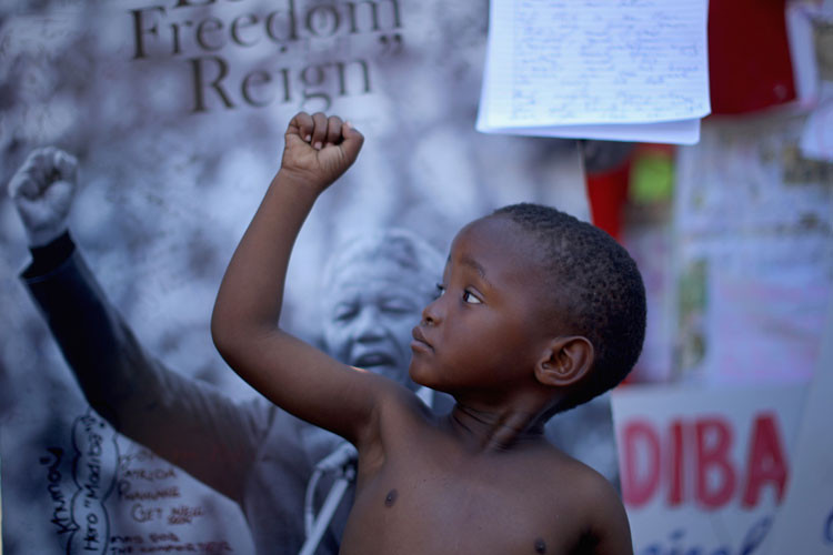 Một bé trai giơ cao nắm đấm, bắt chước hình ảnh chân dung của cựu Tổng thống Nam Phi Nelson Mandela ở bức tưởng tưởng niệm ông bên ngoài Viện tim Medi-Clinic ngày 14/7.