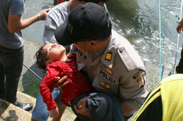 Một cảnh sát Indonesia bế trên tay nạn nhân nhí đang đã bị kiệt sức sau vụ đắm thuyền ở Cidaun đảo Java của Indonesia ngày 24/7 khiến 3 người chết, 157 người may mắn được cứu sống còn nhiều người bị mất tích.