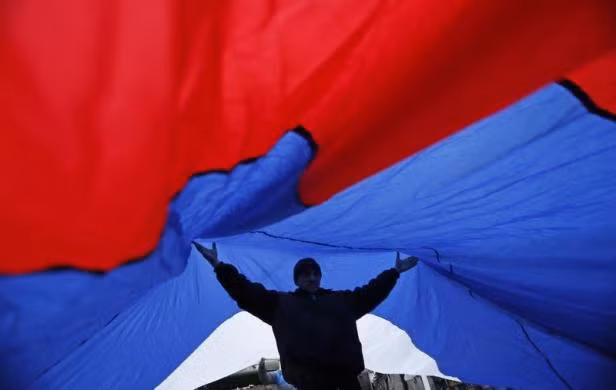 Một người biểu tình ủng hộ Nga giơ 2 tay nâng cao lá cờ Nga khổng lồ ngày 27/2 tại Simferopol.