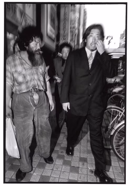 Một thành viên Yakuza đi ngang qua một người vô gia cư ở khu trung tâm tài chính Shinjuku, Tokyo. Ảnh: Bruce Gilden/ Magnum Photos.