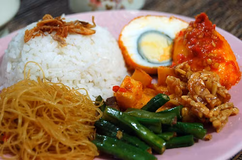Nasi Uduk hay còn gọi là cơm nước cốt dừa, tên gọi này xuất phát từ cách chế biến của món ăn. Ngoài hương thơm dậy của chén cơm nấu cùng nước cốt dừa, Nasi Uduk còn mời gọi du khách với hàng loạt món phụ khác như thịt tẩm gia vị, cá, thịt gà, trứng luộc, xốt ớt và bánh quy giòn.