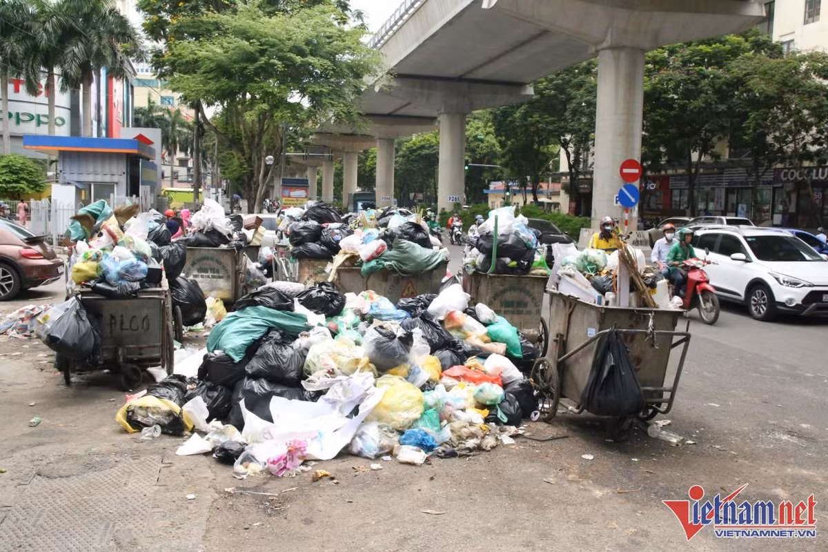 Trên tuyến đường Xuân Thuỷ, rác thải ùn ứ đã nhiều ngày nay. Vào chiều 17/6, công nhân môi trường thu gọn những chiếc xe gom, chờ xe tải xử lý rác thải đến