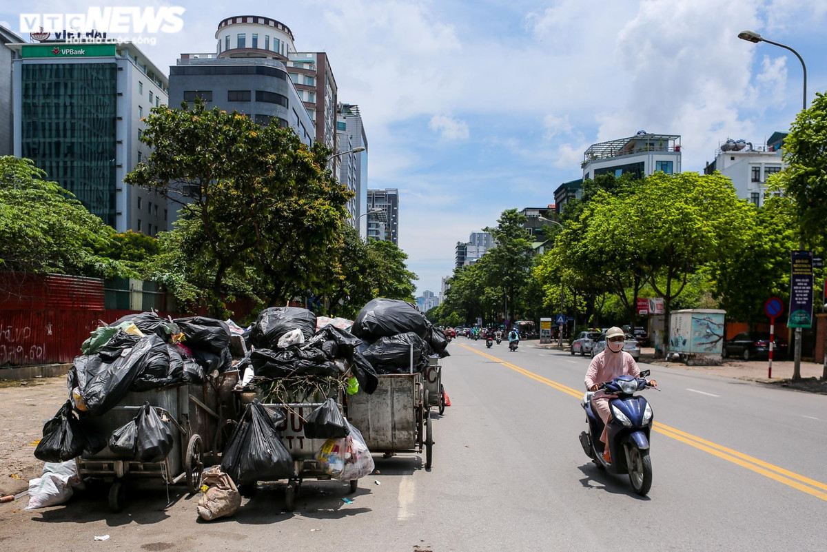 Trong ngày 16/6, trên tuyến đường Duy Tân có hai điểm tập kết rác lớn mà vẫn chưa có hướng xử lý. Tại điểm tập kết rác ở số 4 Duy Tân, có khoảng 15 xe gom chất đầy rác thải để dưới lòng đường.