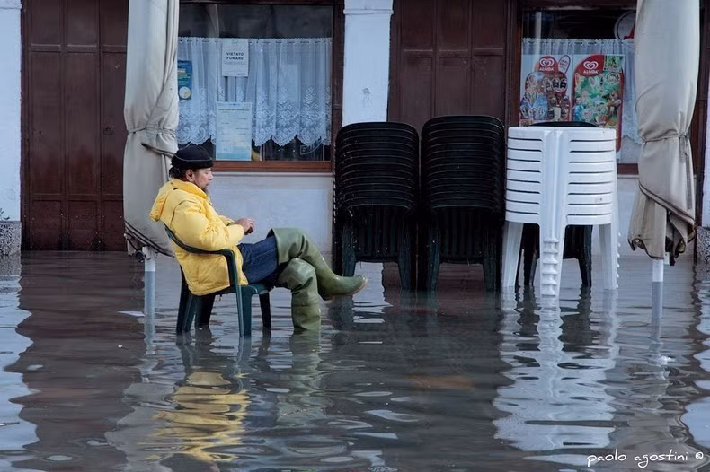 Một người đàn ông bắc ghế ngồi giữa biển nước.
