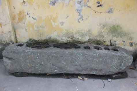 Hòn đá hình chữ nhật, một mặt có khắc 11 lỗ vuông đang đặt trong đình Vạn Phúc.