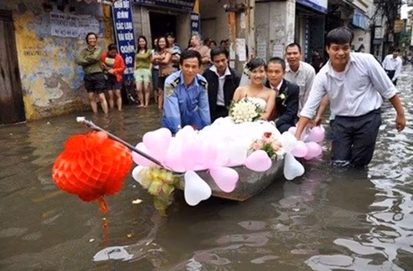 Ảnh chụp lại đám cưới của cô dâu tên Minh Nguyệt và chú rể tên Thành Khánh. Do nước lũ ngập tận vào nhà cô dâu, nên chú rể phải nhờ một chiếc thuyền chở đôi uyên ương ra phía chiếc xe đón dâu. (Ảnh: VOVNews)
