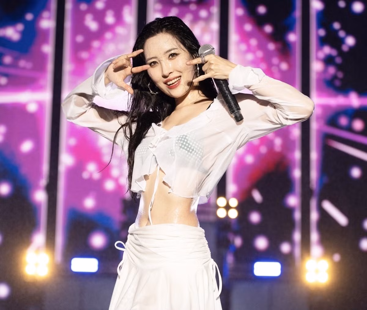 Sunmi mặc áo sơ mi dài tay dáng croptop cùng chân váy trắng, bên trong là nội y màu xanh trông cá tính và gợi cảm.