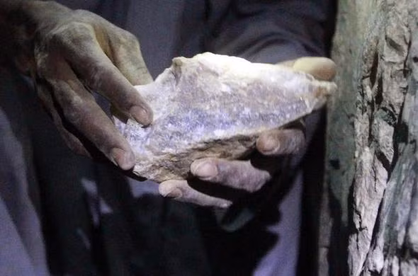 Một công nhân hạnh phúc bên một tảng đá vàng bên trong mỏ.