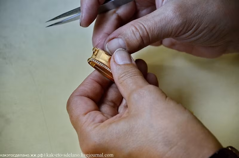 Các nhân viên của nhà máy dùng nhíp để chấm một mảnh vàng nhỏ chấm vào vaseline để gắn hai bộ phận của chiếc đồng hồ.