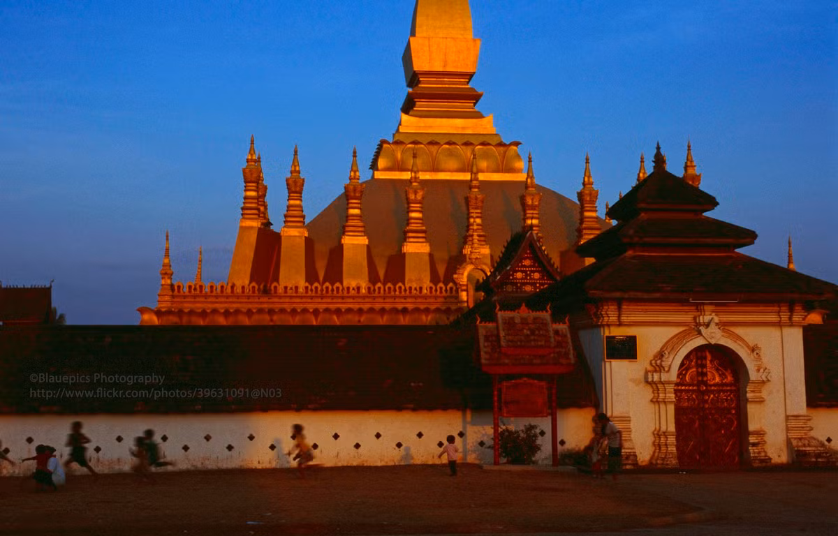 Trẻ em chạy nhảy bên ngoài chùa That Luang lúc hoàng hôn.