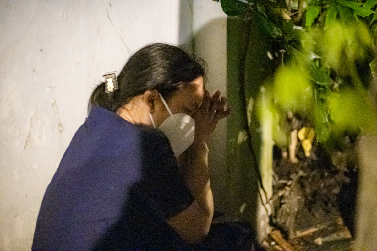 Một phụ nữ ngồi núp sau bóng cây khóc nấc thương xót người thân, ánh mắt chị thâm quầng sau khi nước mắt đã cạn.